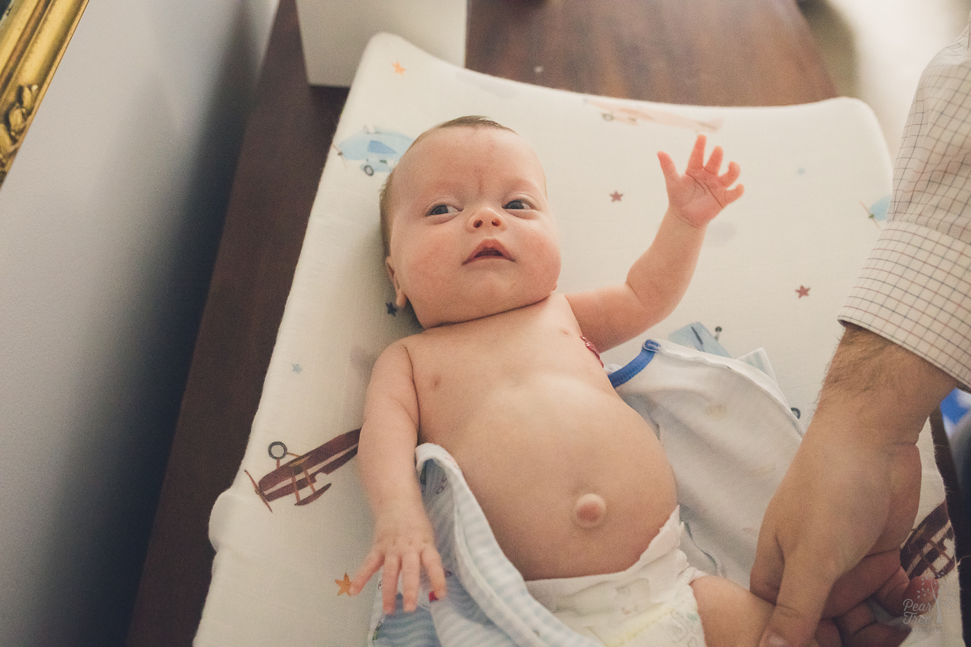 Baby boy with outtie belly button laying on a changing table with his arms reaching out for delayed newborn photographs
