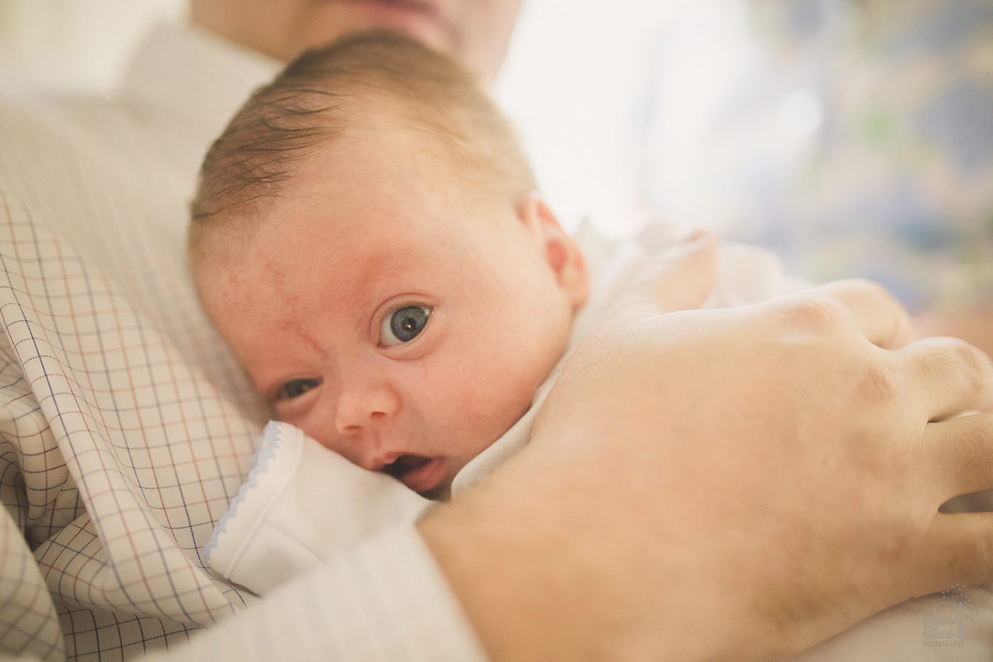 Newborn baby being held by his dad with one eye wide open