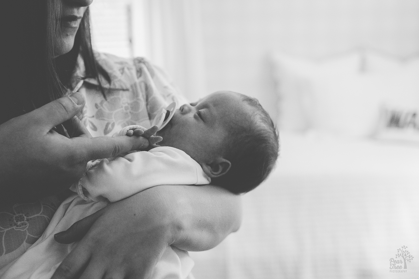 Black and white photograph of mom holding newborn son sucking his pacifier. Dad is letting this son hold onto his index finger