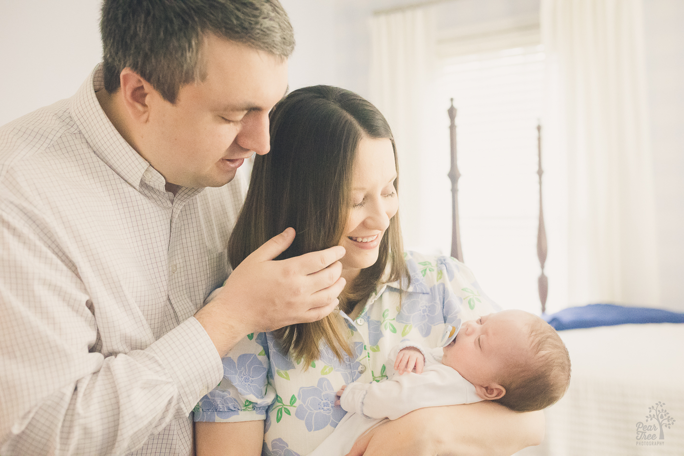 Dad is pulling mom's hair back from her face so he can see their son in her arms for delayed newborn photographs