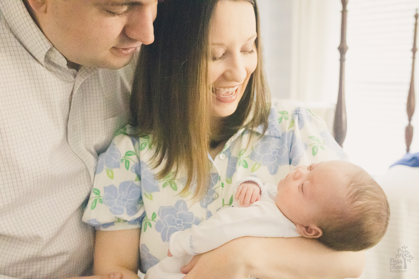 Mom holding newborn baby boy and smiling big while dad leans in