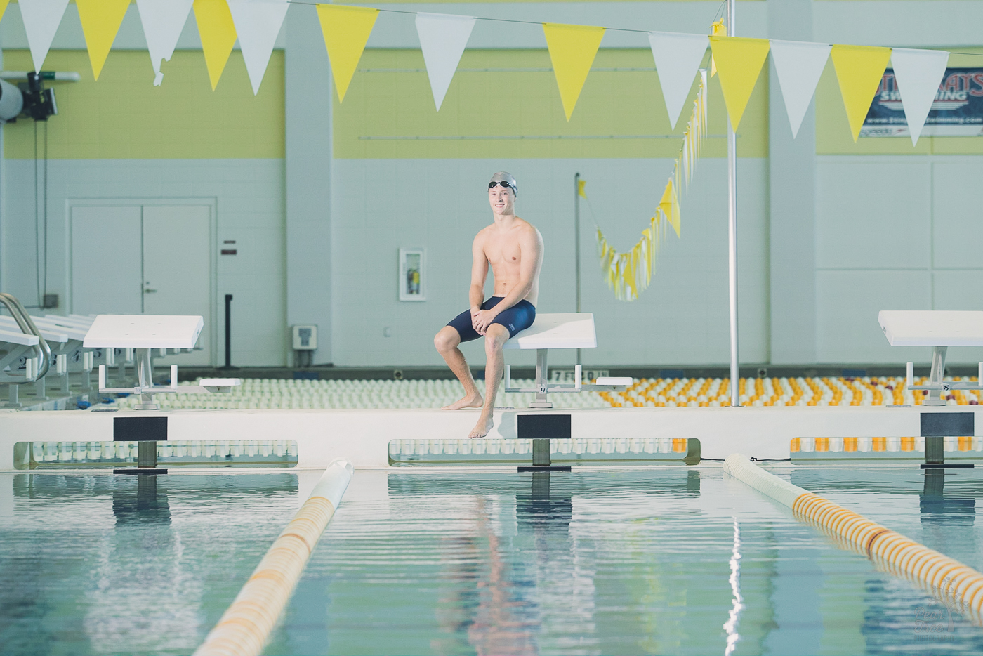 Woodstock high school senior boy swimmer sitting on diving block with his goggles pushed up over his swim cap