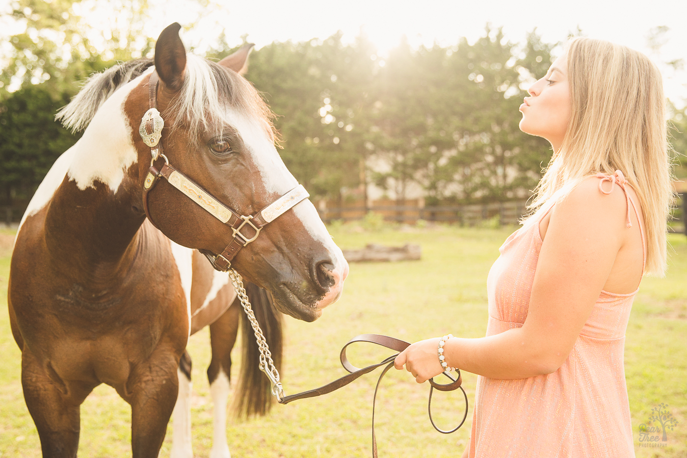A pretty blonde girl in a pink dress making a kissing face for senior photographs with a horse