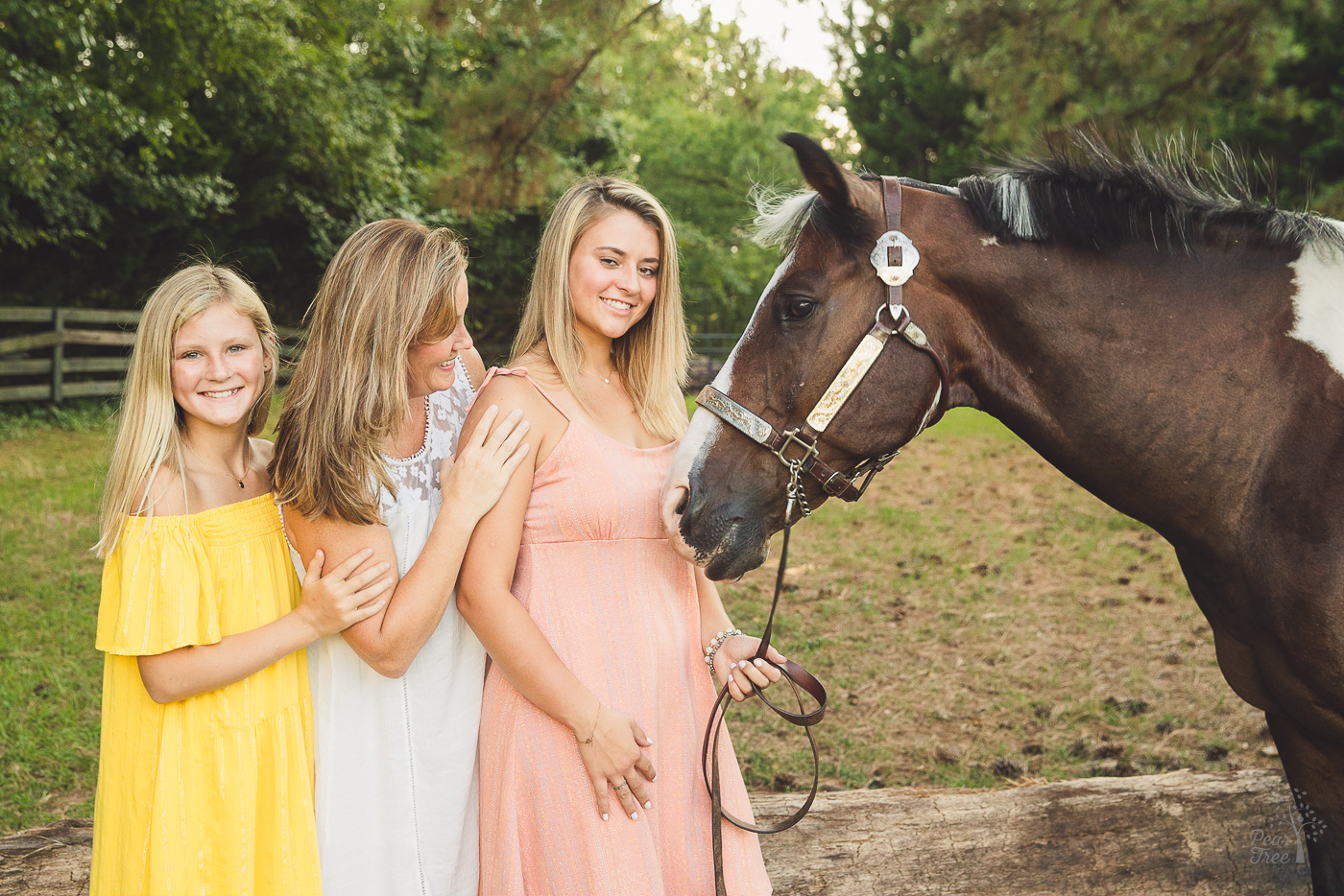 Little sister in yellow dress holding her mom's arm. Mom is smiling at horse and has her hand on her high school senior daughter's shoulder