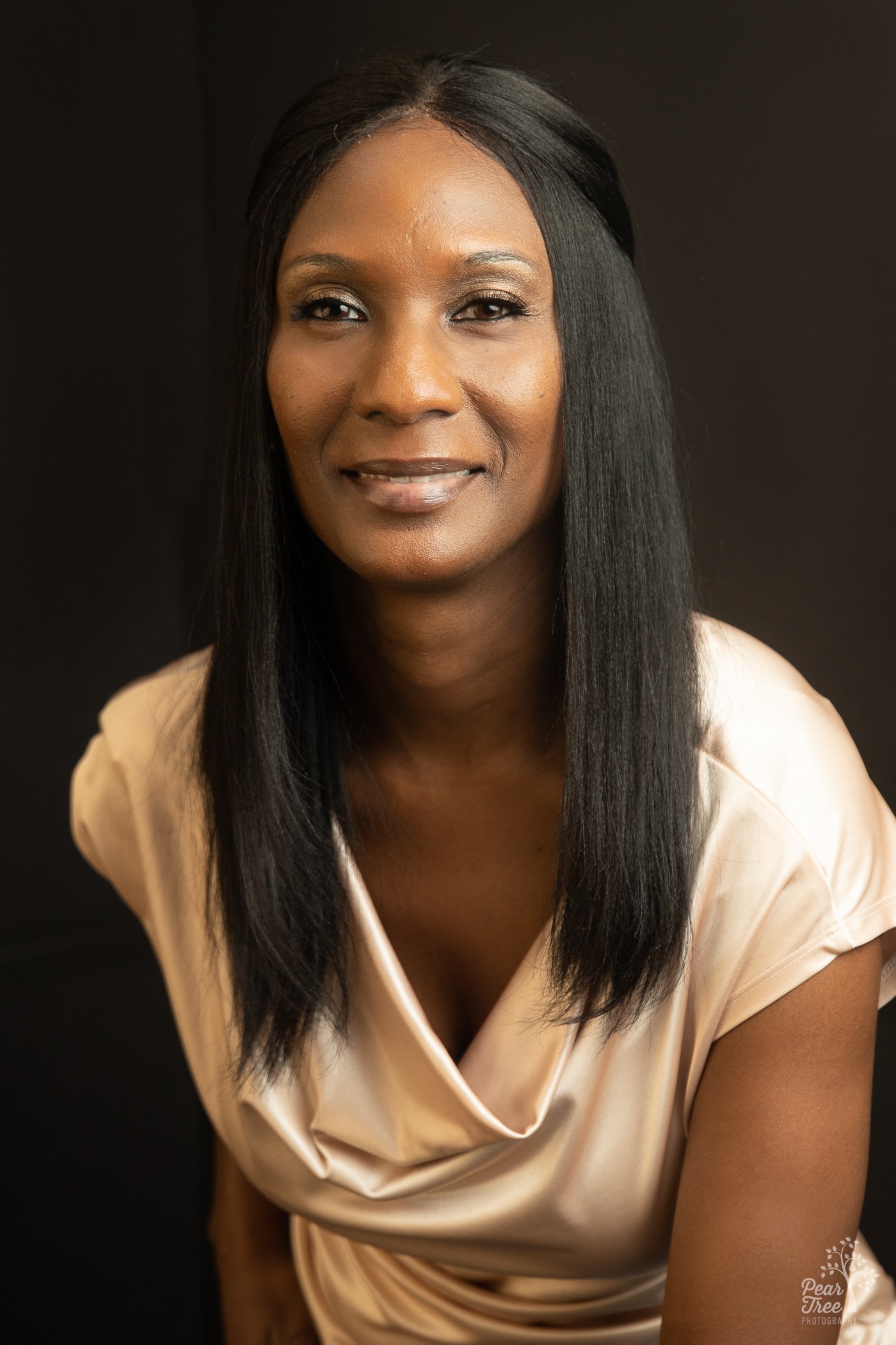 Professional headshot in Canton of an African American woman smiling while wearing a pearl shirt and leaning towards the camera