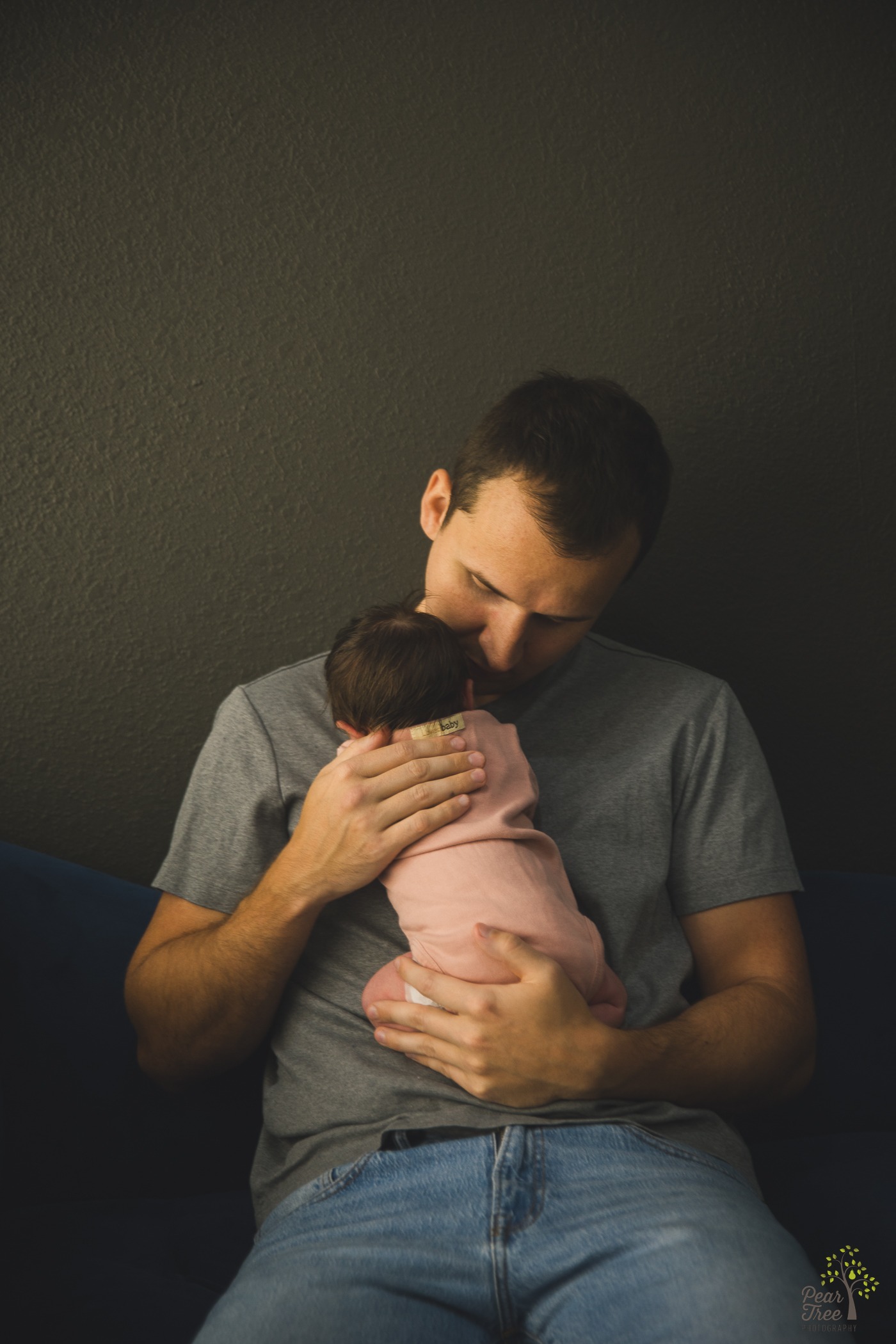 Father holding his newborn daughter while he sits leaning against a wall