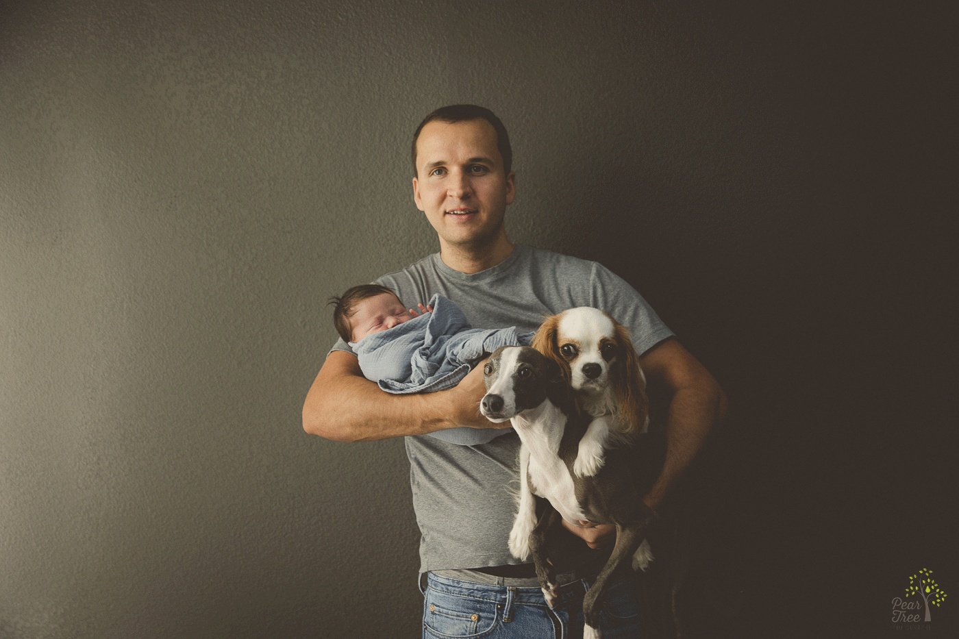 Dad holding his newborn baby girl, miniature greyhound, and a King Charles dog in both of his arms