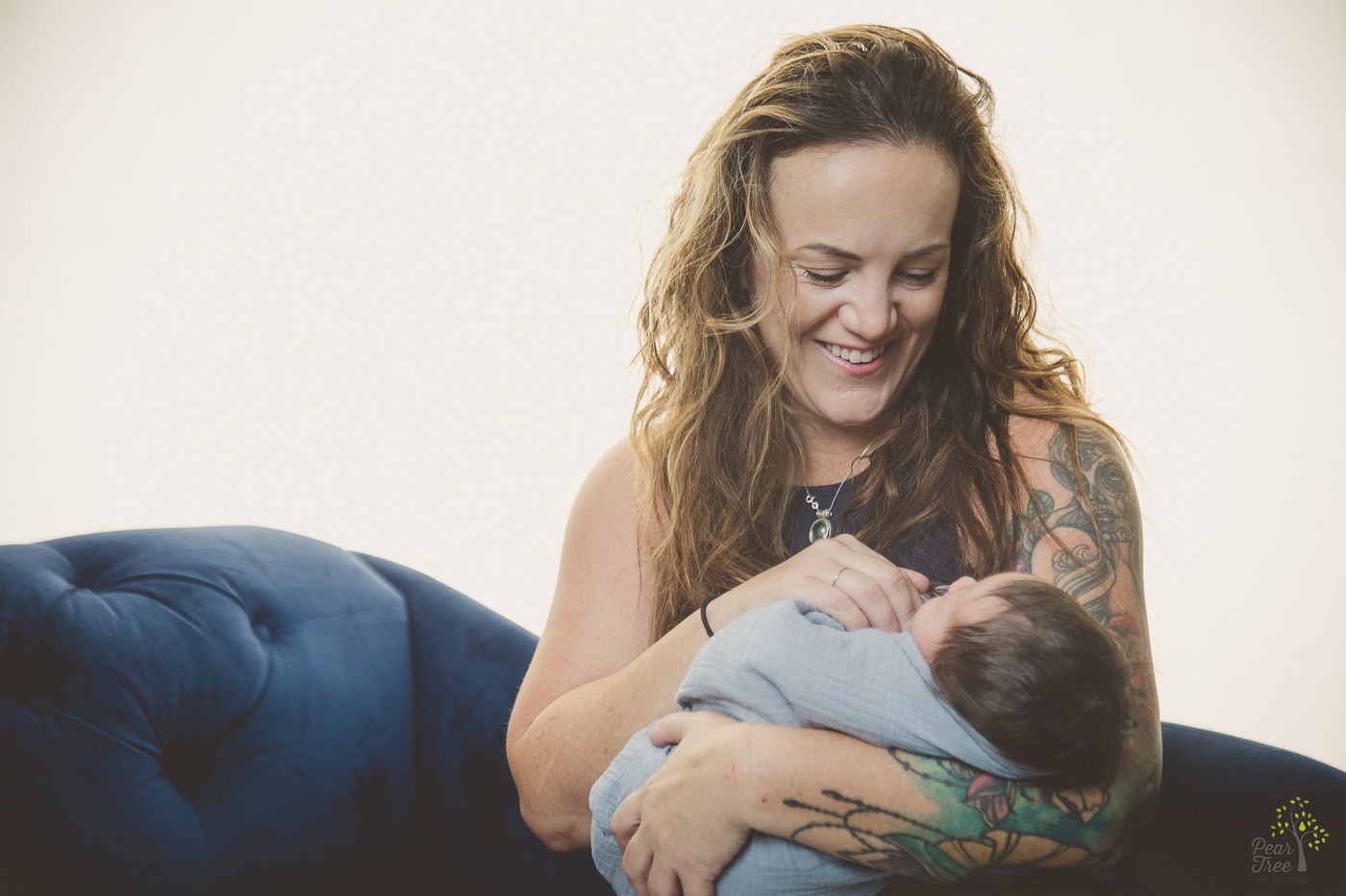 Young grandma with tattooed sleeve on upper arm holding her newborn grand daughter and smiling