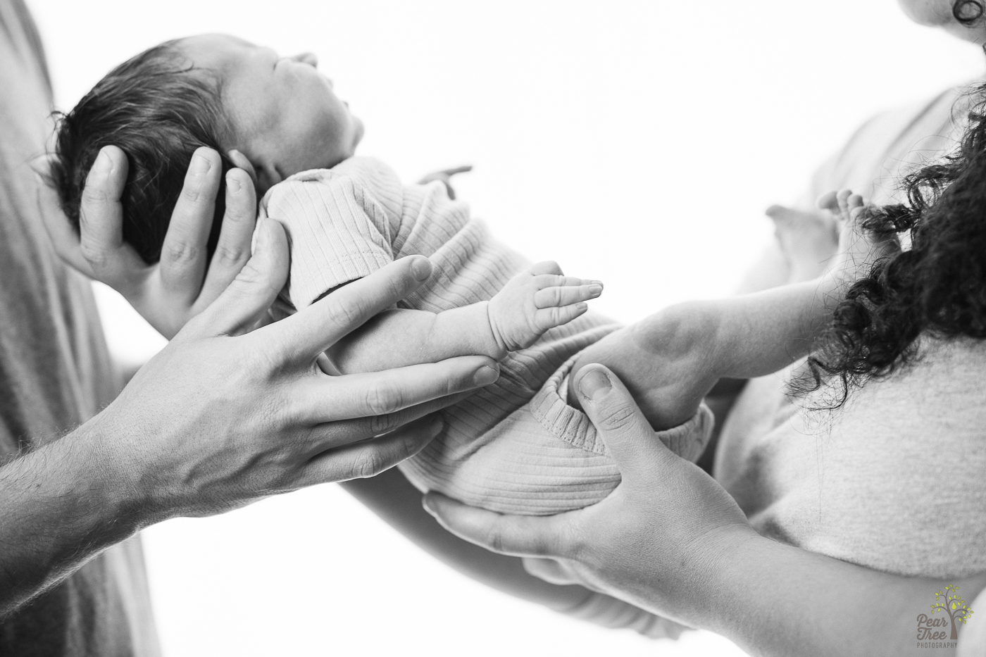 Black and white photograph of parents hands holding newborn daughter between them