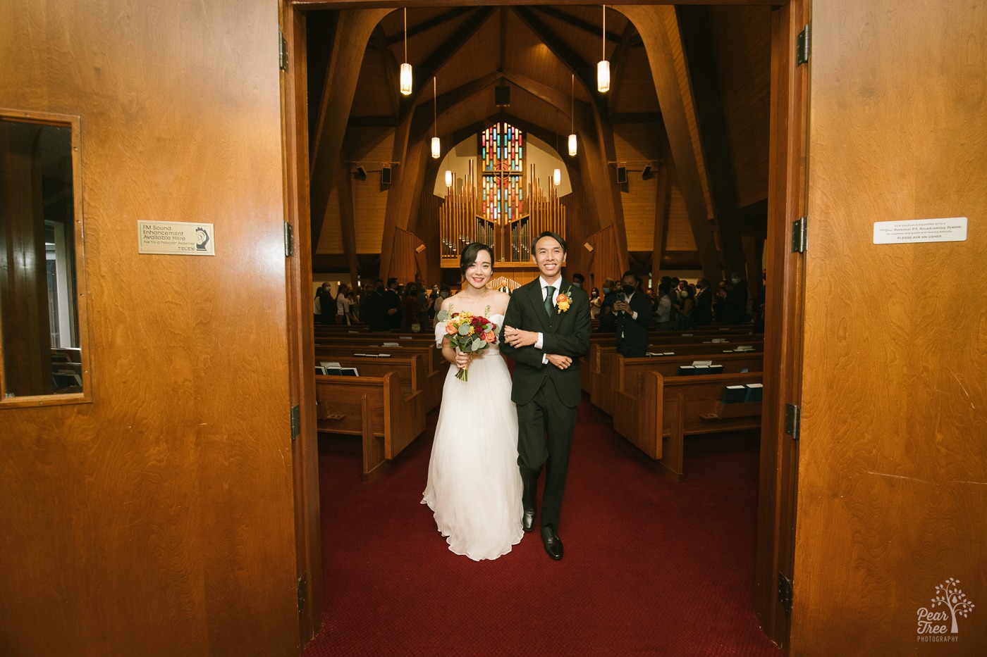 Asian wedding couple exiting Eastminster Presbyterian Church sanctuary and holding hands
