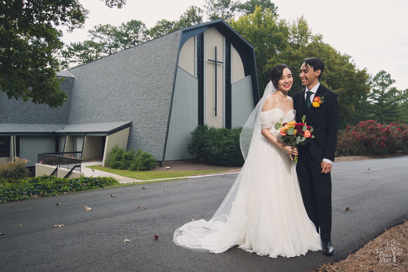 Asian wedding ccouple smiling and standing in front of Eastminster Presbyterian Church in Stone Mountain