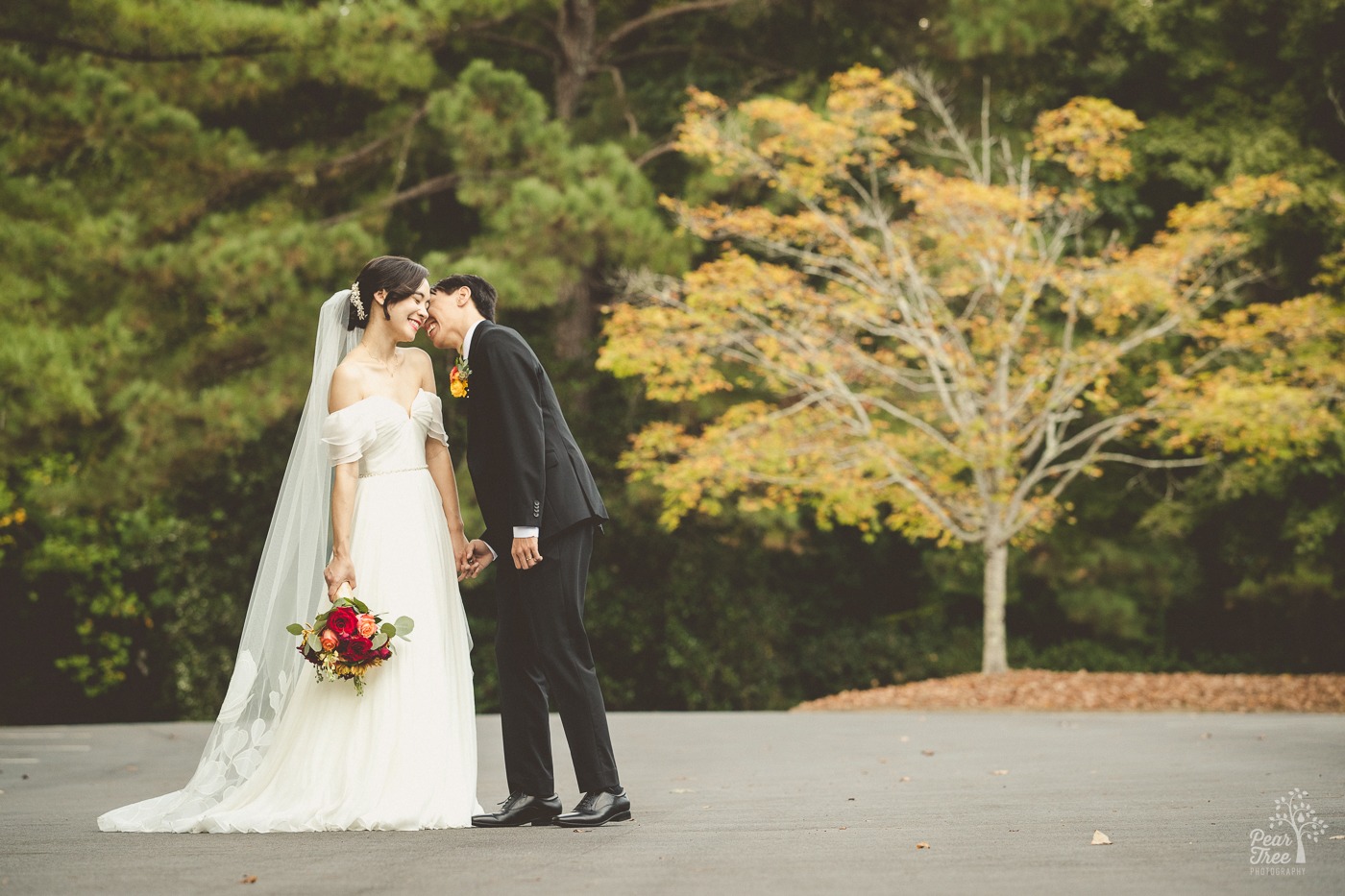 Smiling Asian bride holding a bouquet by her side while her husband holds her hand and laughs