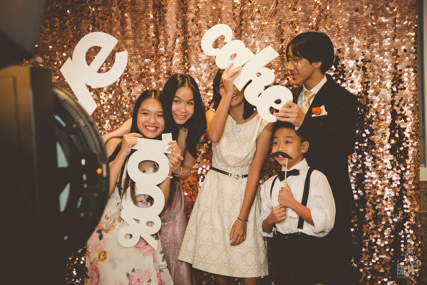 Asian teenagers cheesing in a photobooth in front of a sequin wall