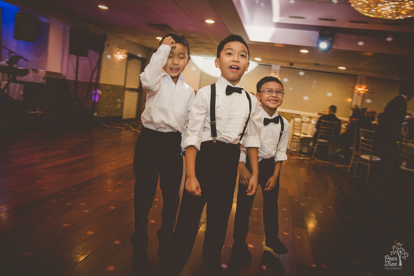 Asian American boys in black pants, white button down shirts, suspenders, and black bow ties laughing