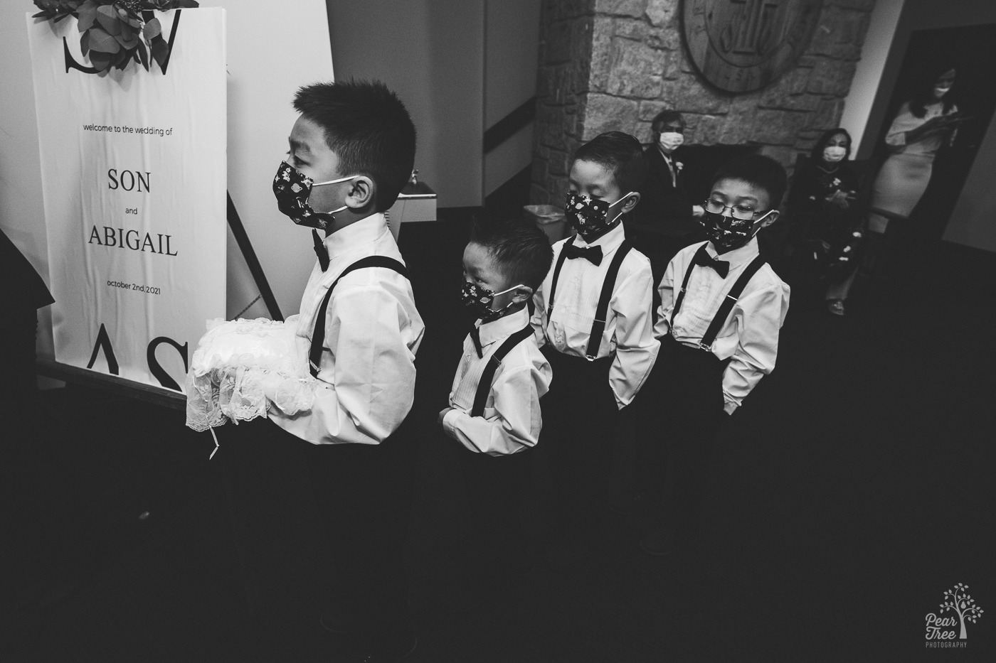 Black and white photo of four young Asian boys in bow ties and suspenders waiting for a wedding to start