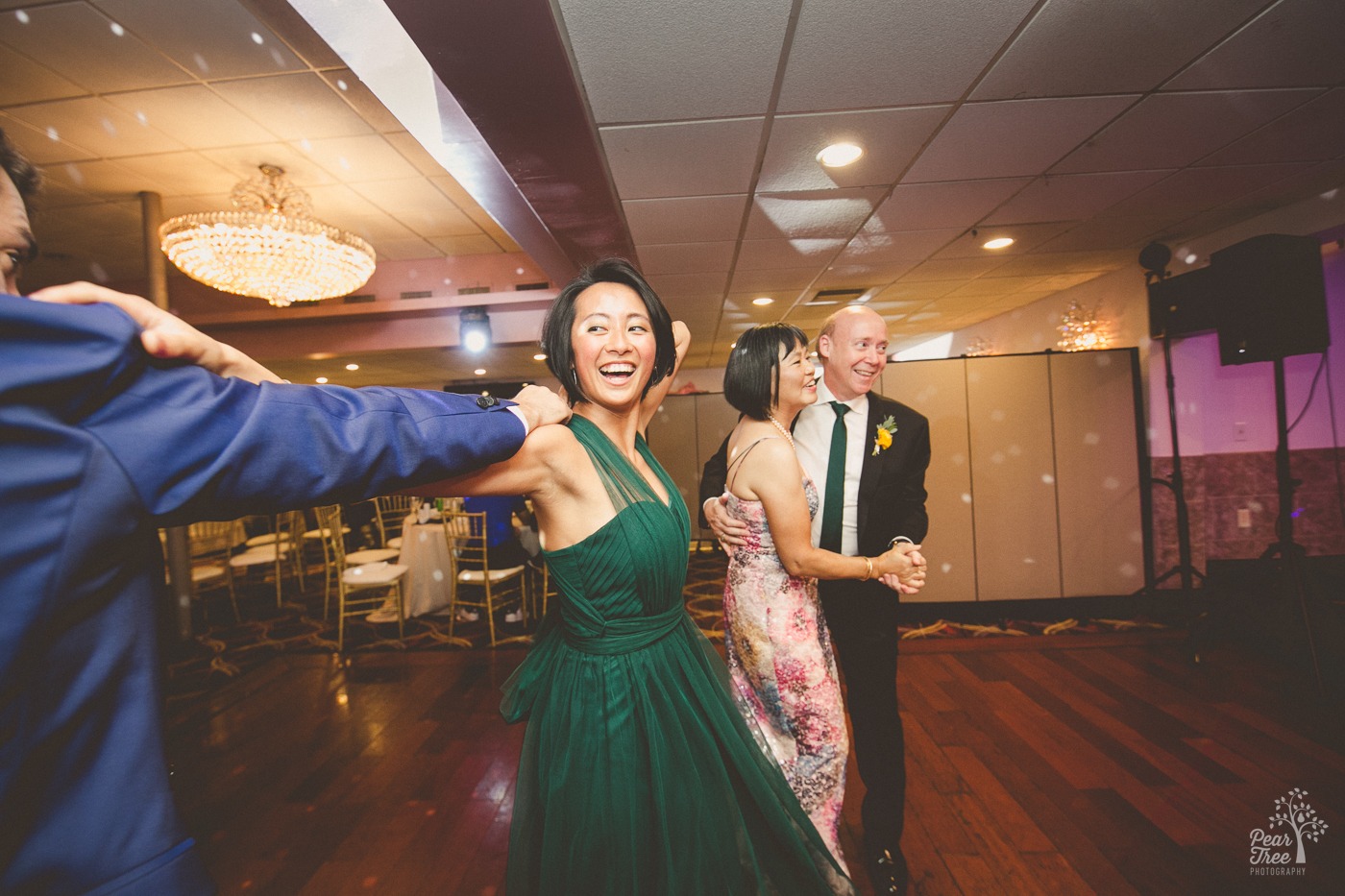 Smiling Asian woman in emerald green dress dancing at wedding reception