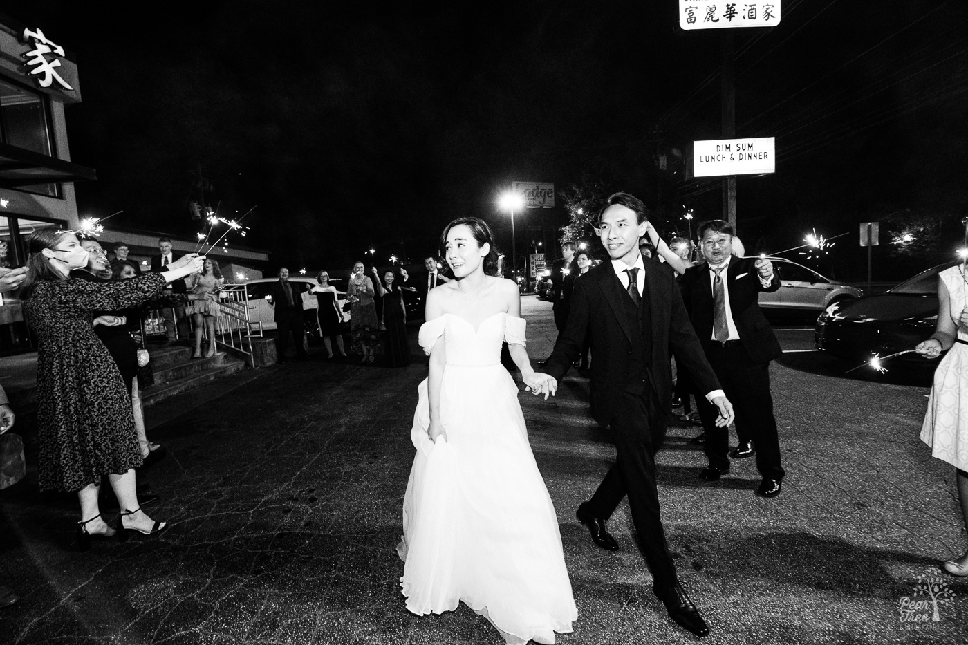 Black and white photo of newlywed Asian couple holding hands while walking through parking lot at night