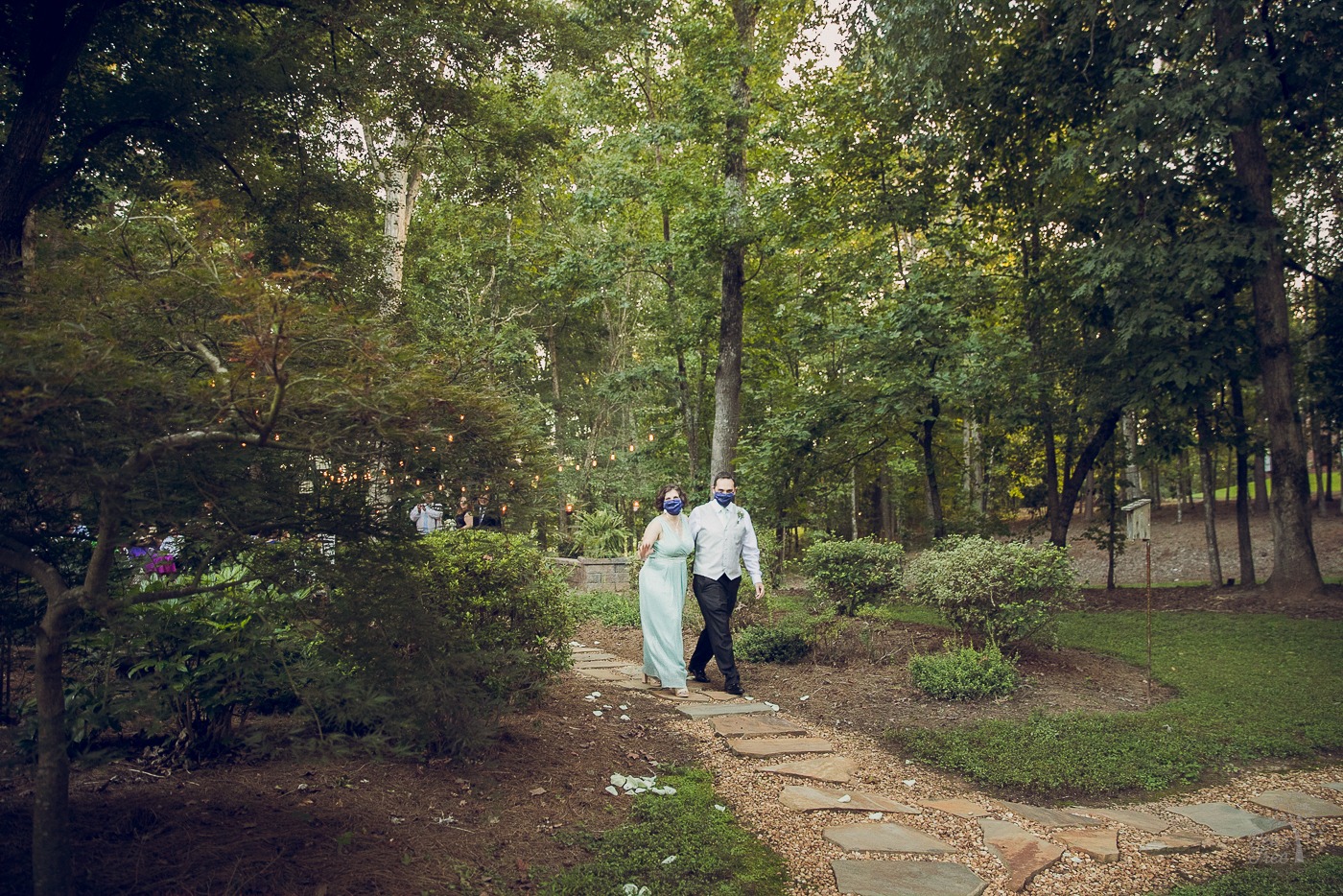 Newlywed couple in masks walking through a backyard after their wedding ceremony