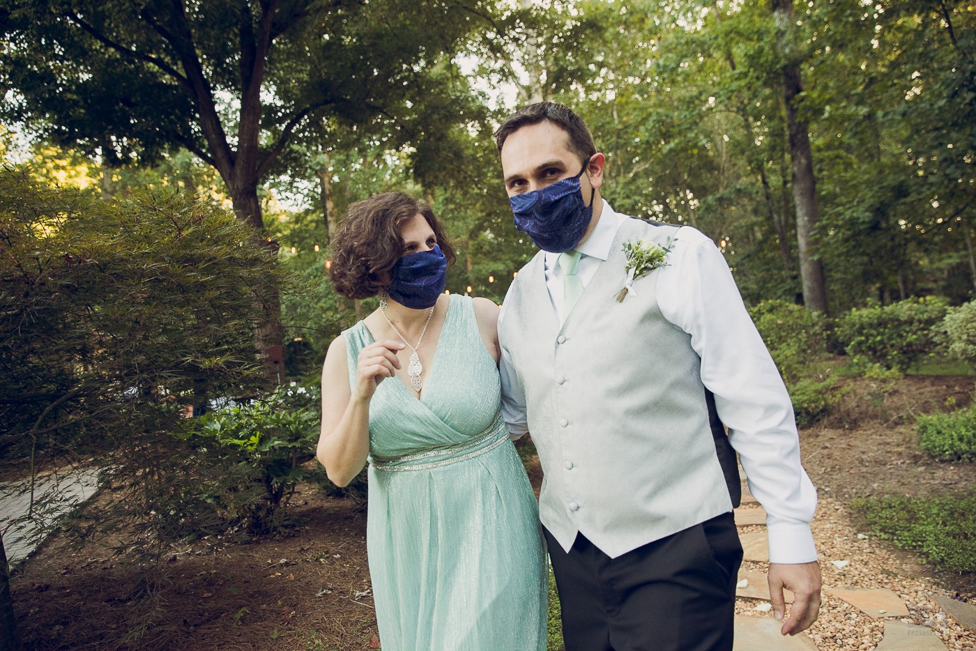 Newlywed couple walking down the backyard aisle in masks