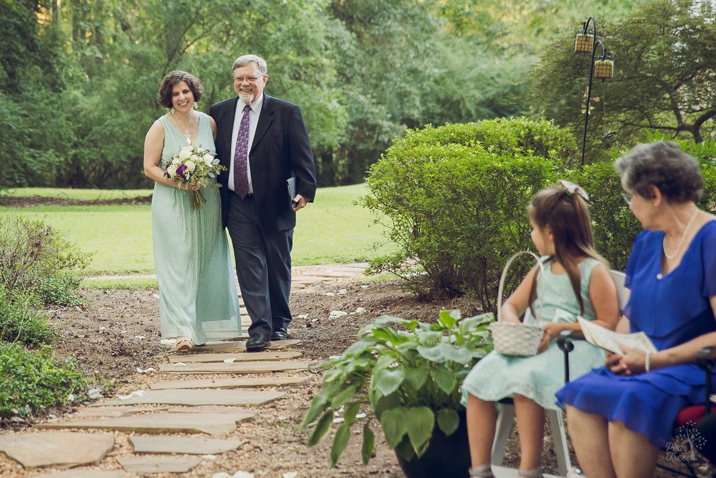 Dad and officiant walking his daughter down a stone path during her wedding in a backyard
