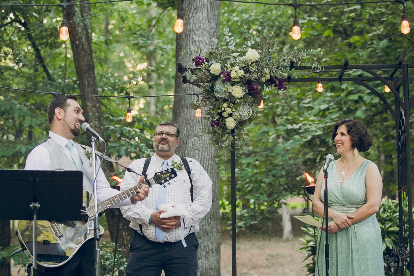 Groom playing guitar and singing to his bride while she watches during backyard wedding ceremony
