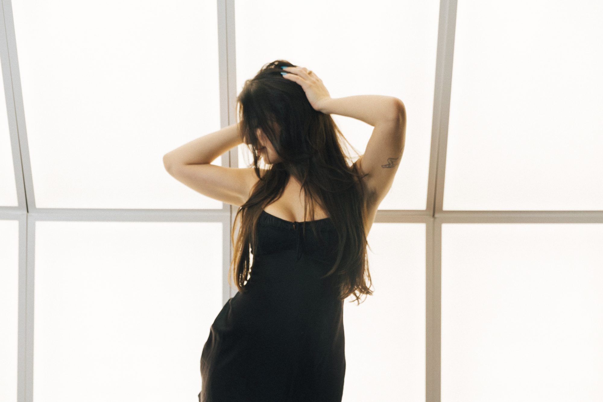 Anonymous woman standing in front of windows with her head turned to the side wearing a little black dress