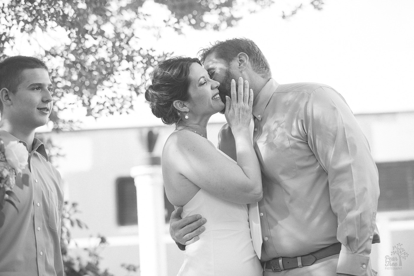 Groom kissing his bride's cheek while she smiles and touches his neck