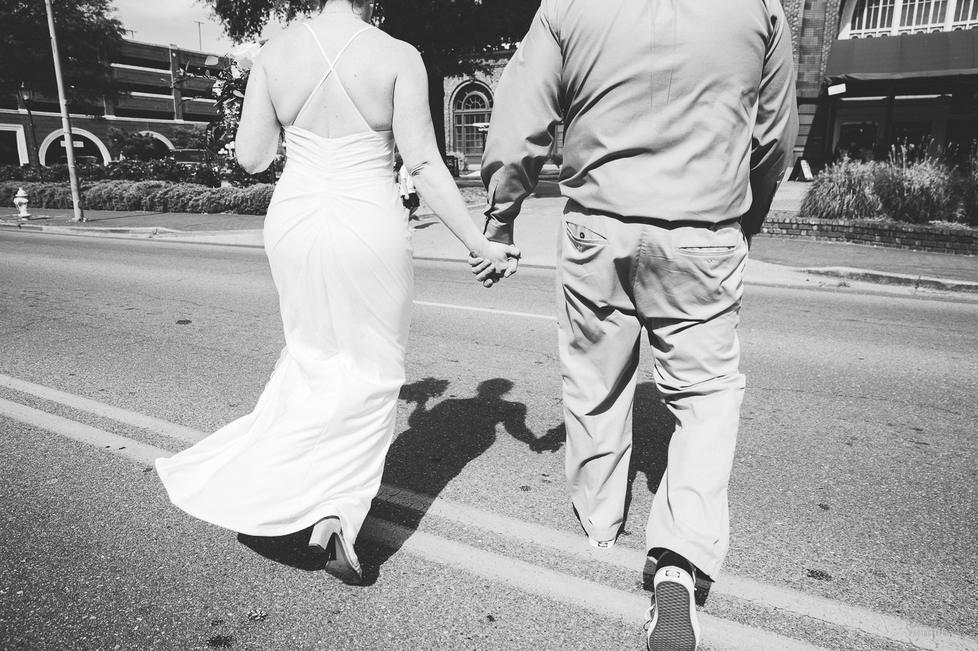 Black and white photograph of bride and groom holding hands while running across the street