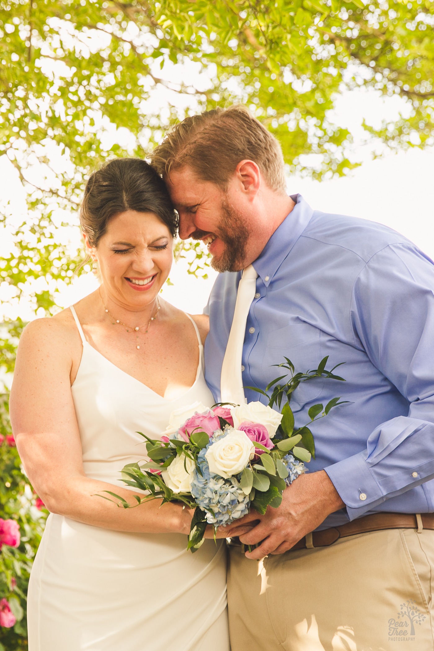 Bride and groom holding flower bouquet and laughing hard