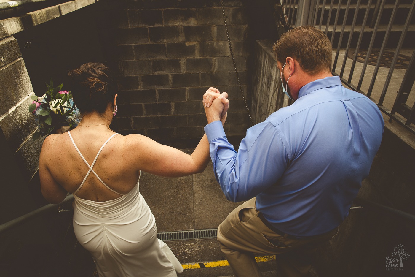 Bride and groom holding hands in air as they walk down steps at Chattanooga Whiskey brewery