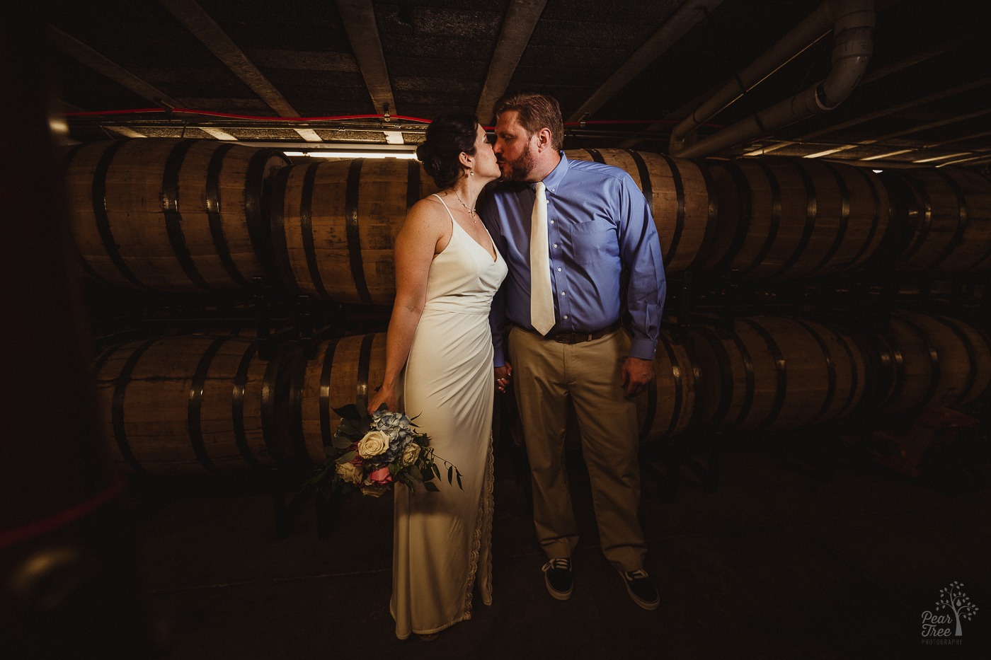 Bride holding bouquet and kissing her groom in Chattanooga Whiskey barrell room
