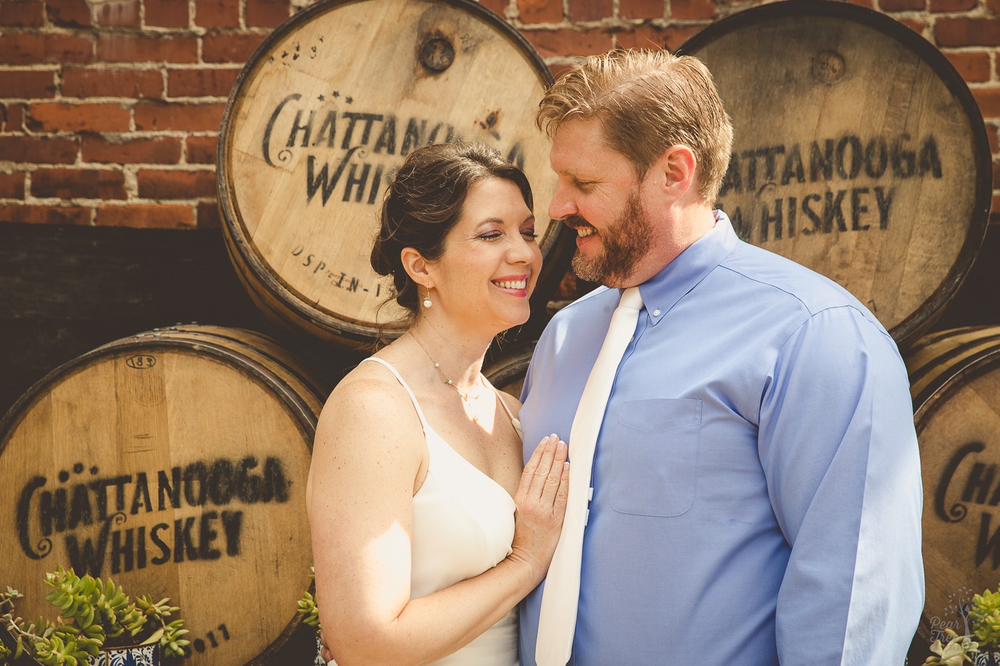 Wedding couple standing close and smiling in front of stacked Chattanooga Whiskey barrels