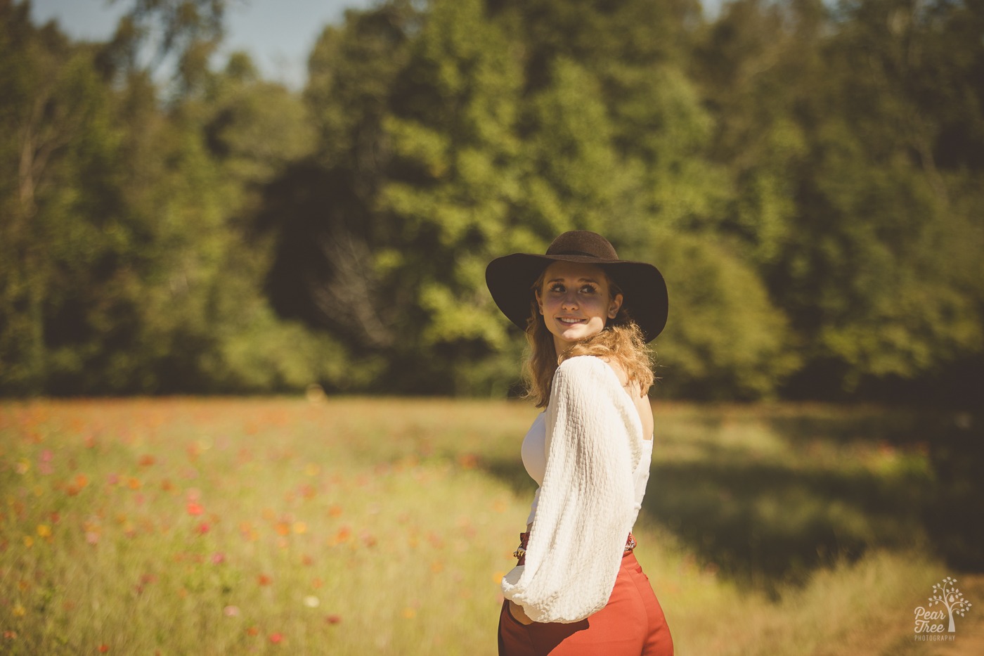 Beautiful oung woman standing in a flower field wearing a hat and looking back over her shoulder