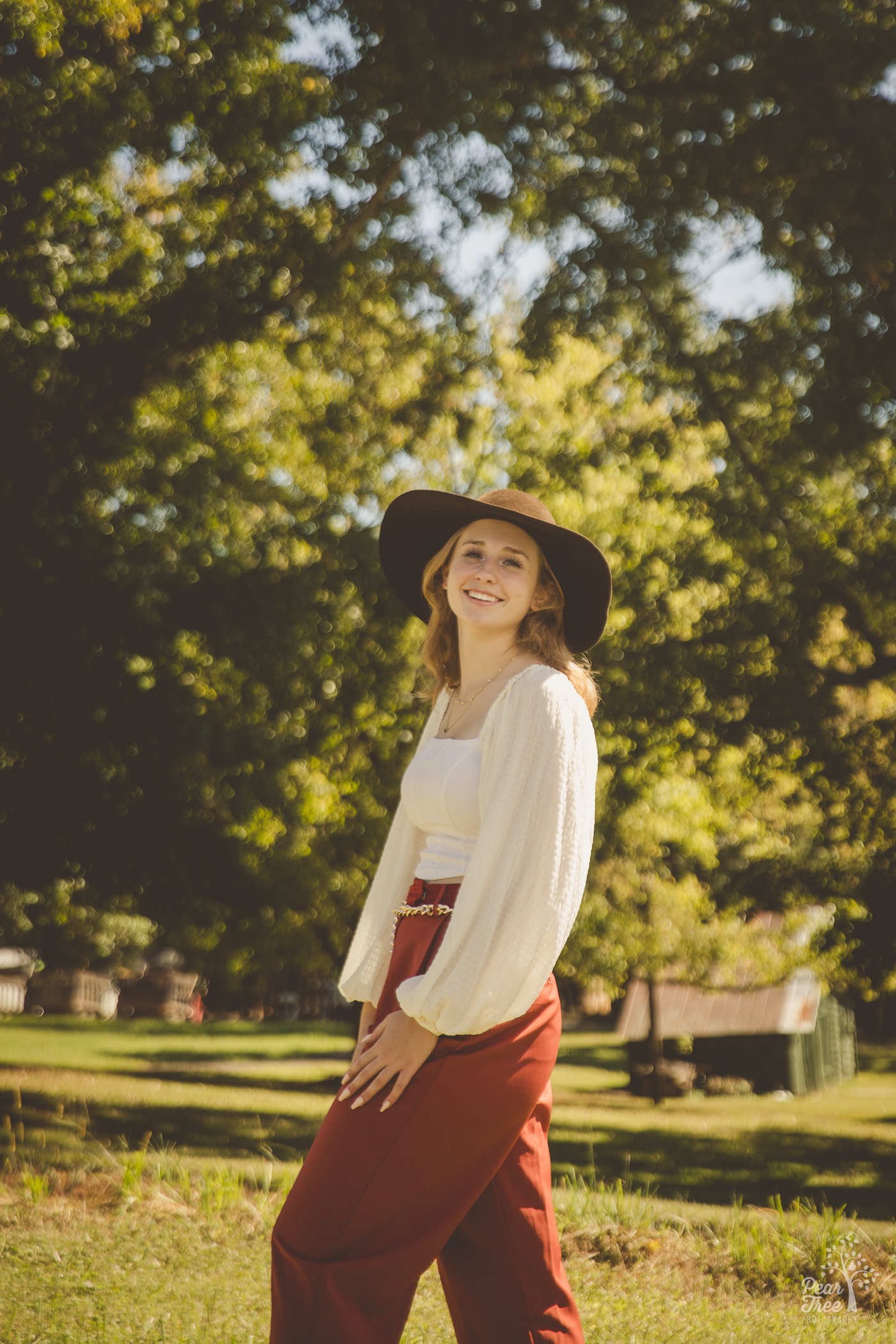 Creekview high school senior girl smiling in a hat in front of tall trees