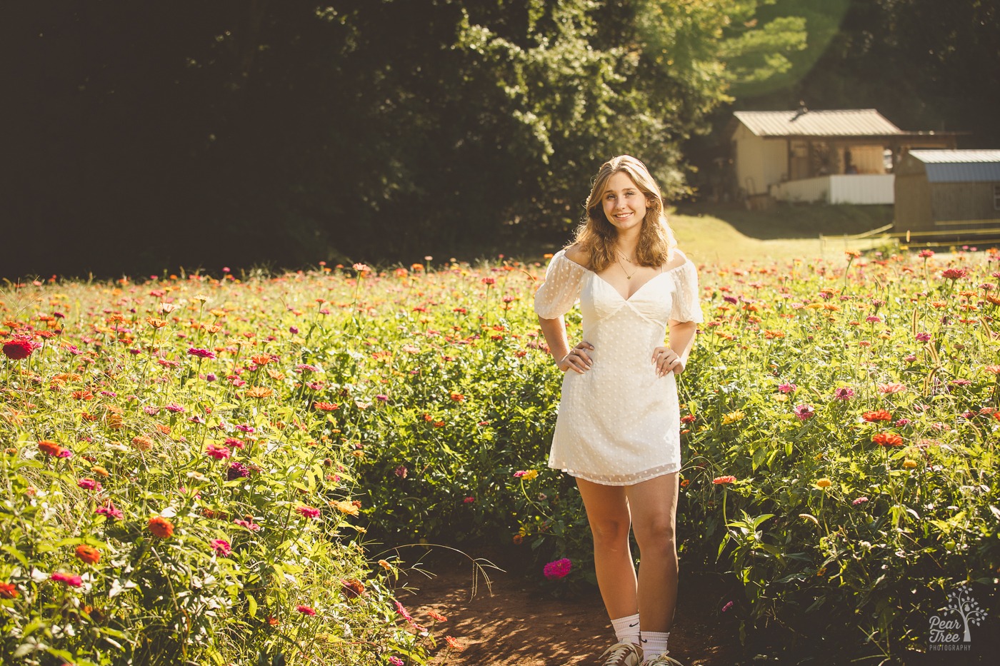 High school senior girl in a white dress and sneakers smiling in a flower field