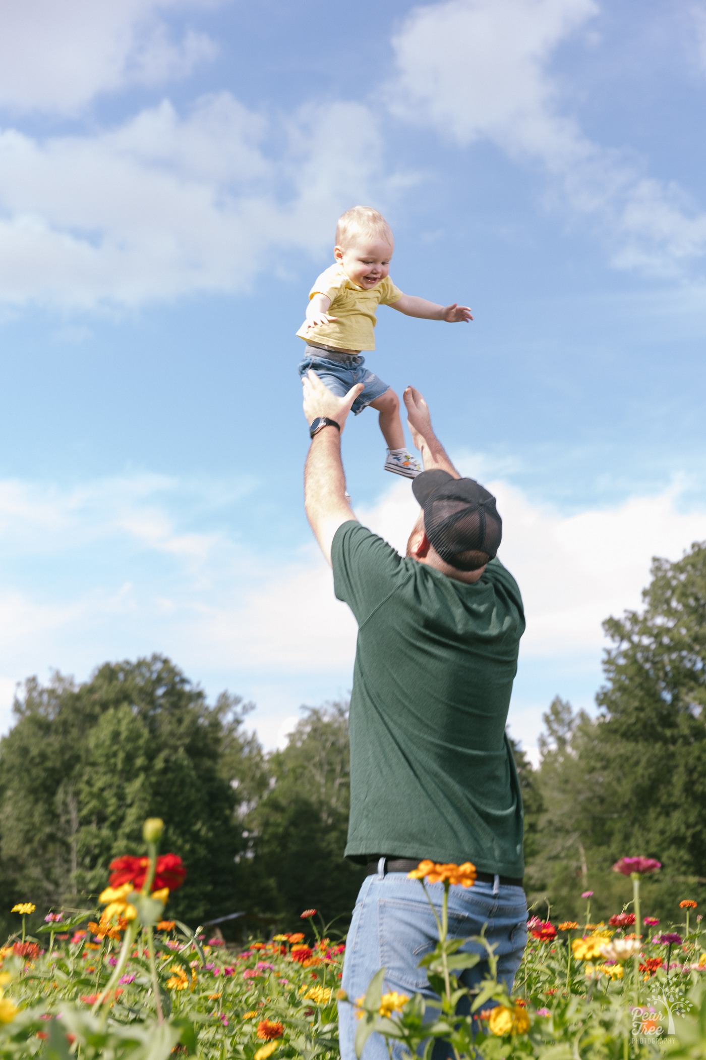 Dad throwing his one year old son above his head in the middle of a wildflower field