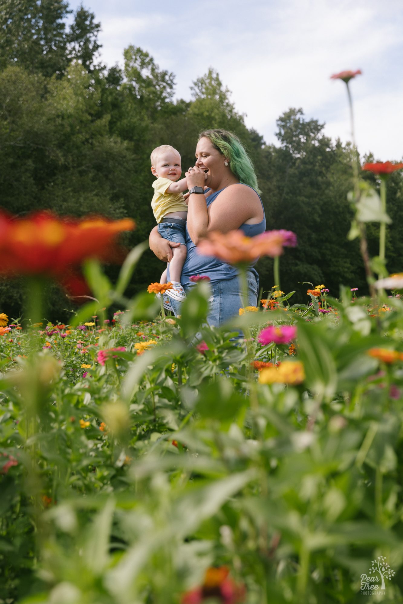 Mom with green hair holding her one year old son in a field of flowers