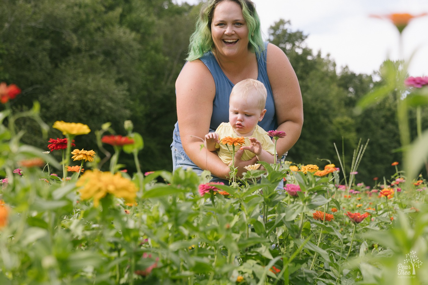 Laughing mom holding her one year old son over wild flowers