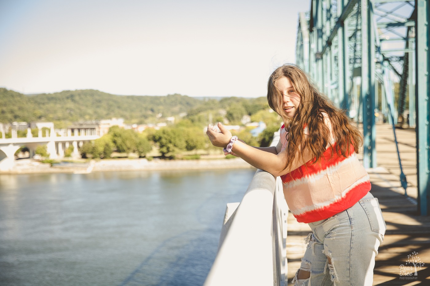 Girl with long brown hair blowing in her face as she leans on Chattanooga bridge