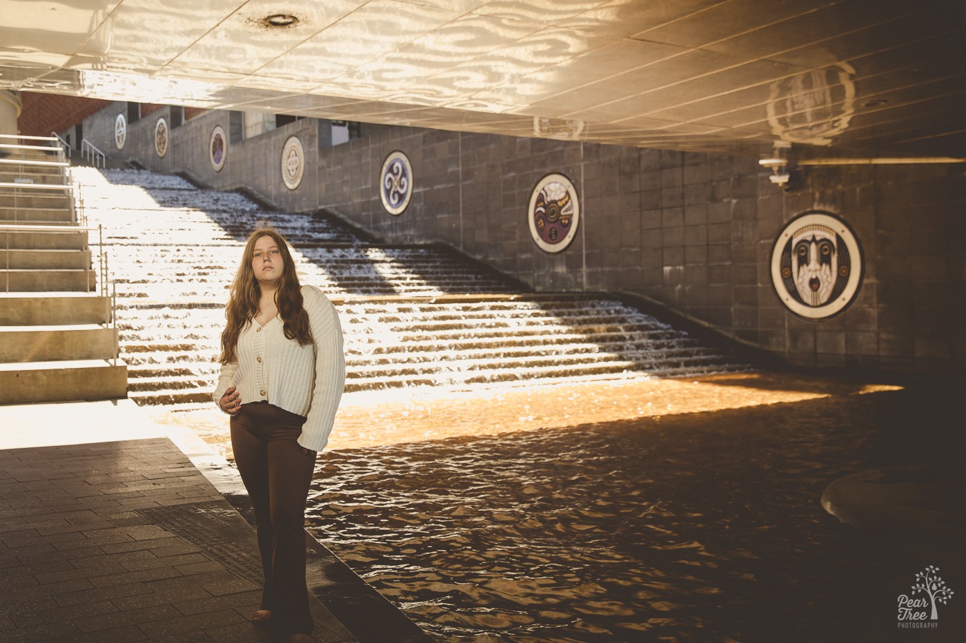 Pretty girl with long brown hair standing seriously in front of waterfall steps in Chattanooga