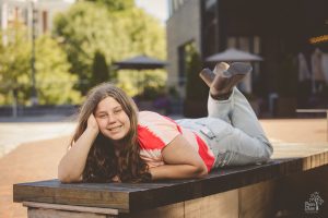 Sweet high school senior girl with long hair laying on a park bench and smiling in Chattanooga
