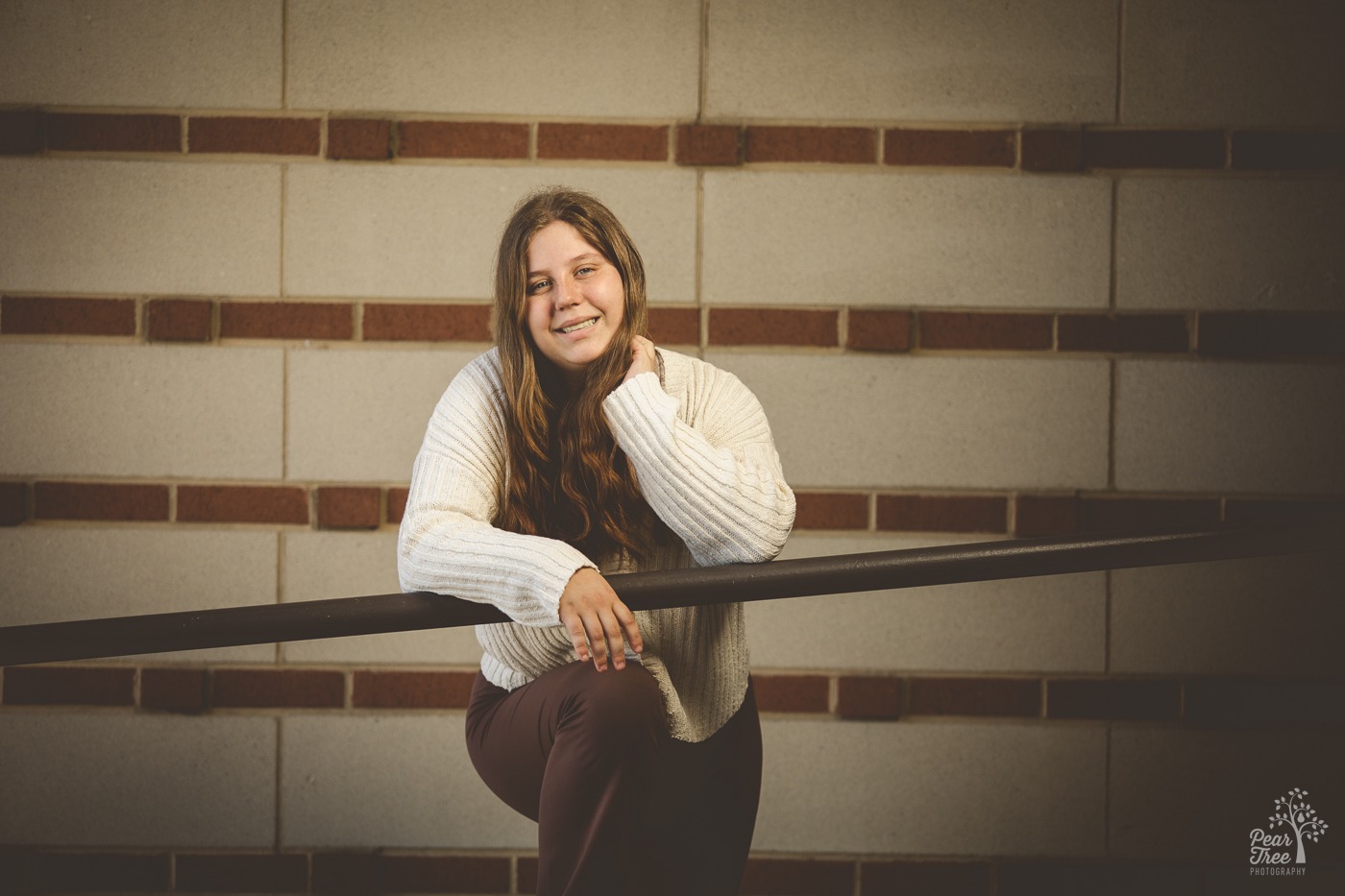 High school senior girl in brown pants and cream sweater leaning over a railing and smiling in Chattanooga