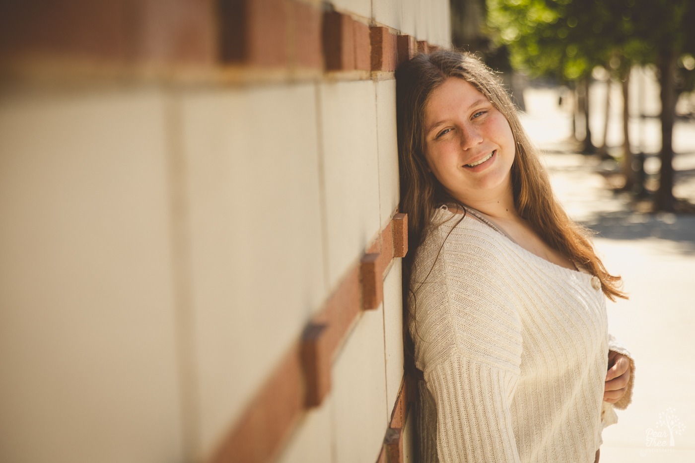 High school senior girl leaning against a cement wall and wearing a cream sweater