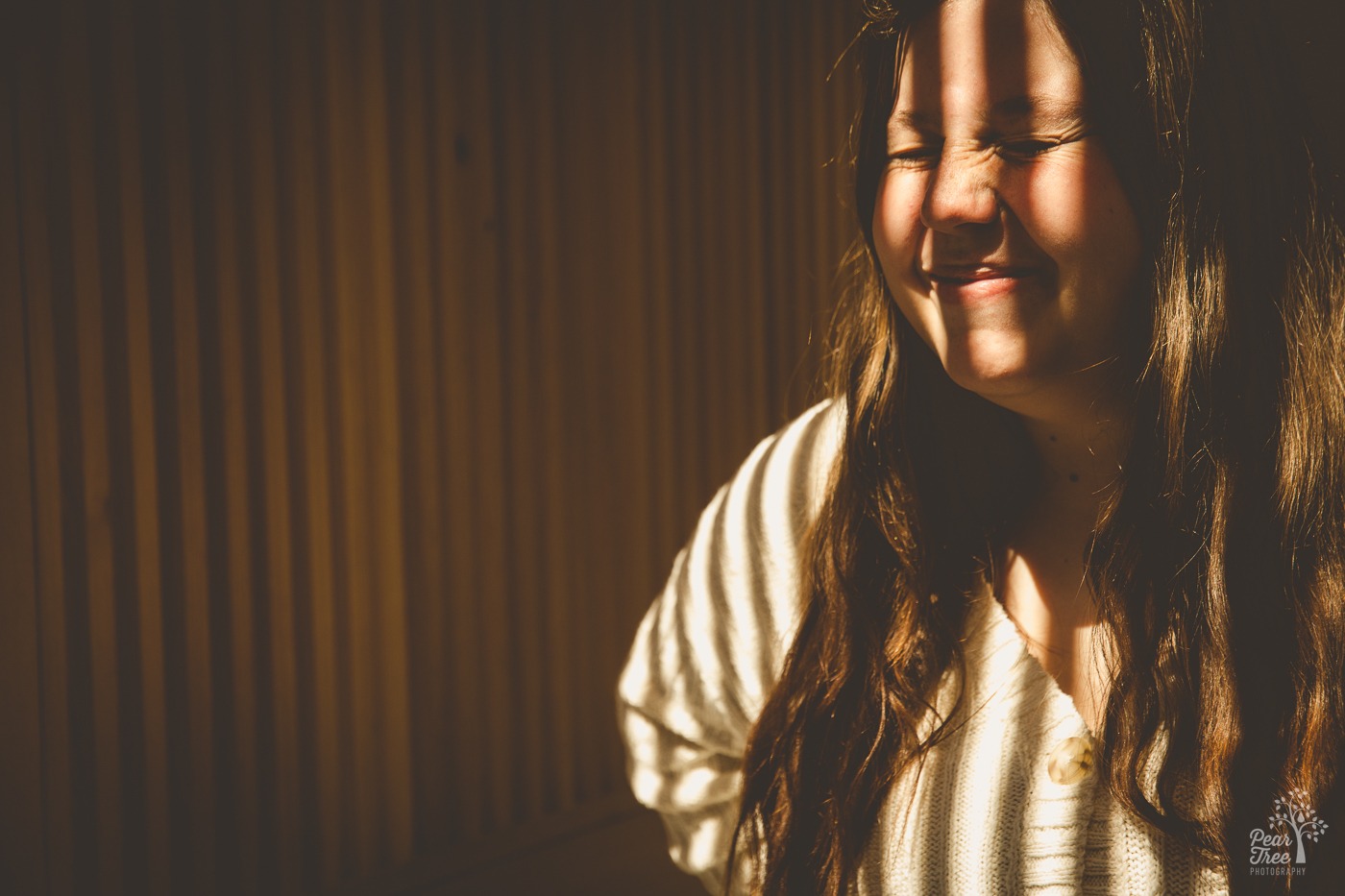 Striped shadows falling over the face of a girl laughing and squinching her eyes shut