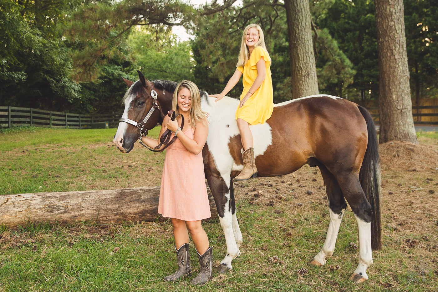 Two sisters in sundresses and cowgirl boots smiling and laughing while standing with their paint horse in Woodstock