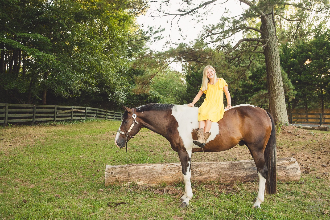 Young girl with long blond hair sitting bareback on her paint horse and smiling in a Woodstock, GA stable pasture