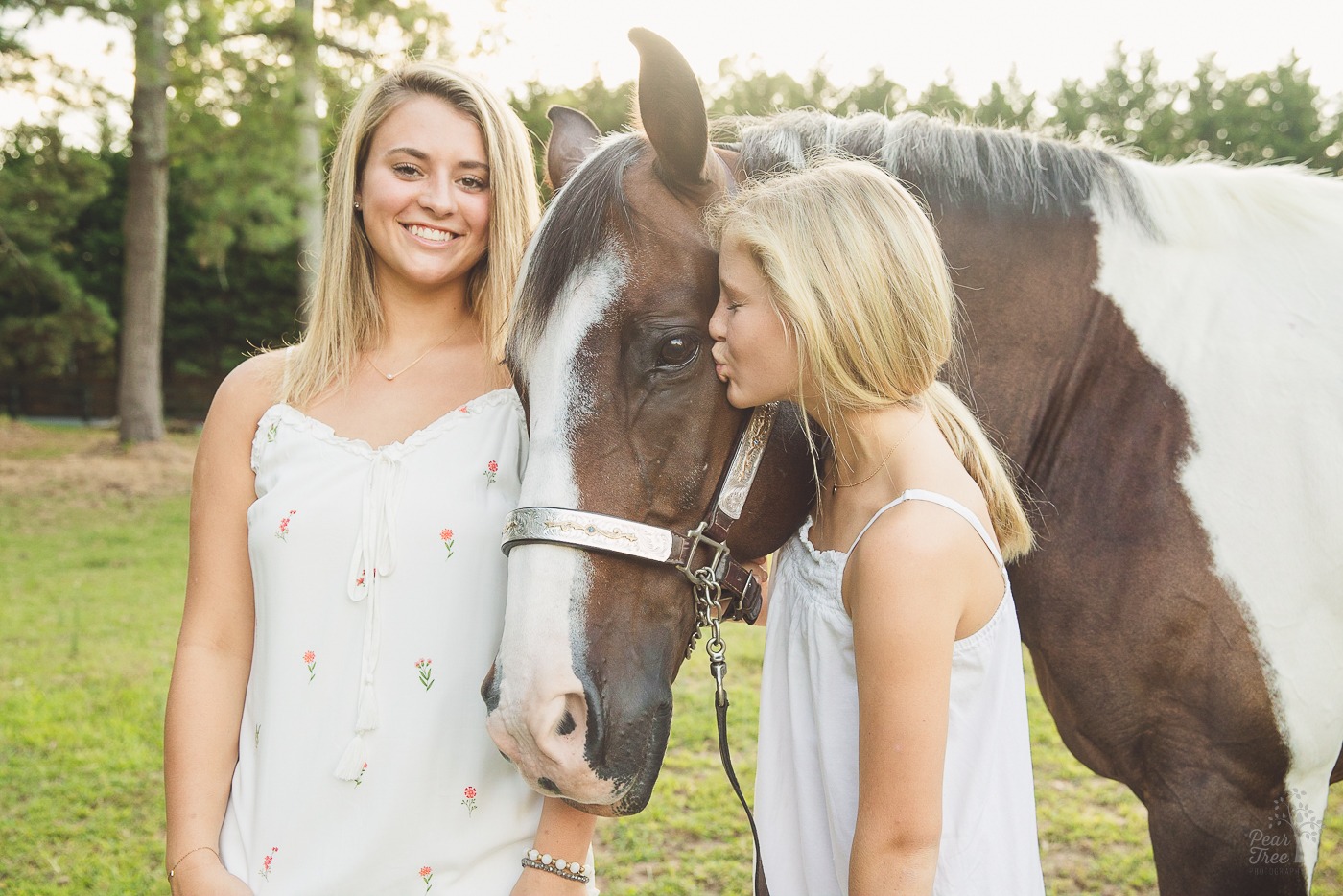 Two sisters with their paint horse. One is smiling and the other is kissing him just below his eye