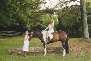 Two sisters in white sundresses and cowgirl boots in a Woodstock field with their paint horse