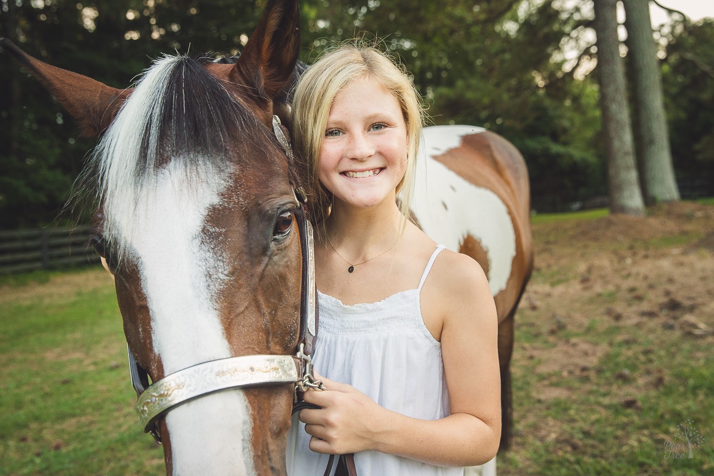 Happy girl in a white sundress holding her paint horse close