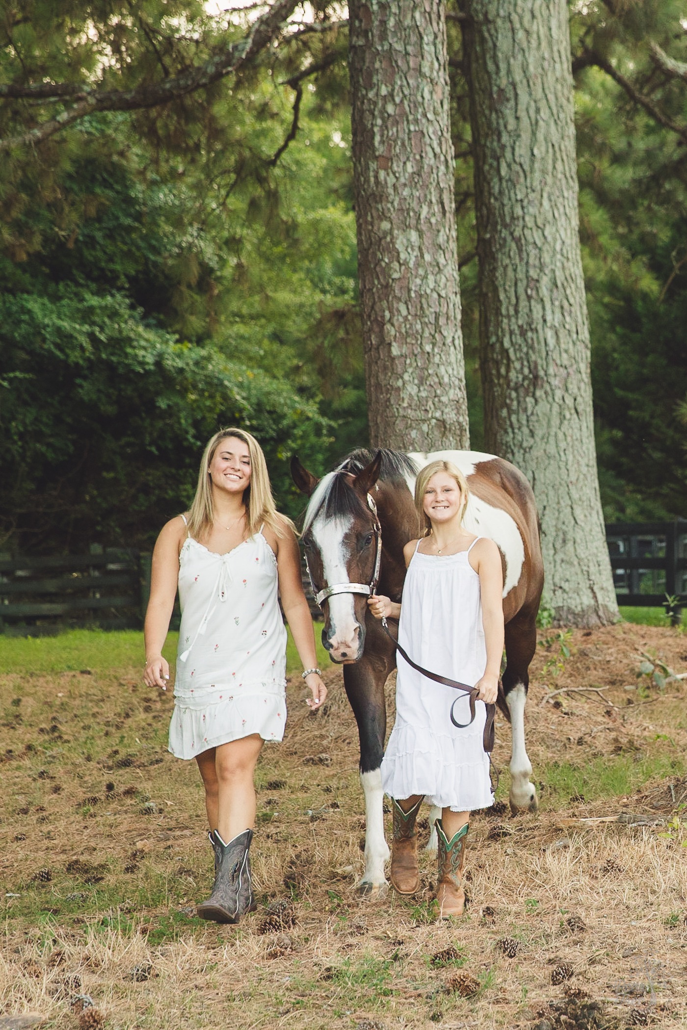 Two sisters smiling while walking their paint horse on a lead past trees